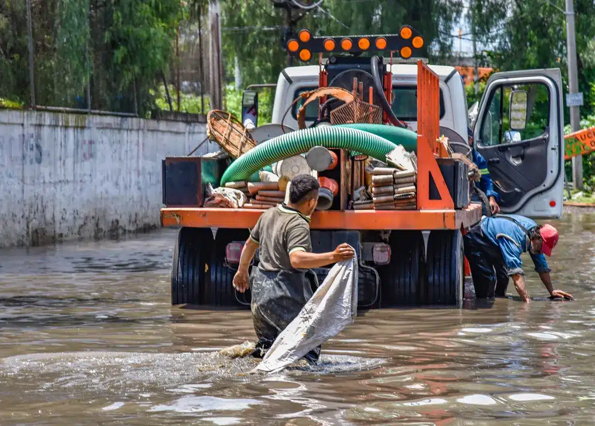 Equipos de emergencia trabajando en una calle inundada con árboles derribados y daños en infraestructuras