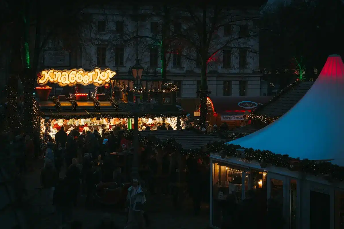 Multitud de personas disfrutando en una plaza festiva con cervezas, iluminación nocturna y ambiente de celebración veran