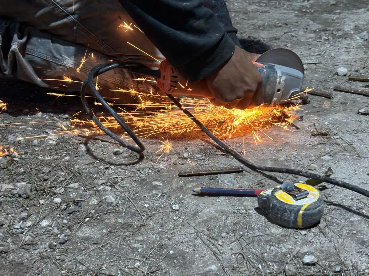 Trabajador usando amoladora en demolición cerca de vegetación seca