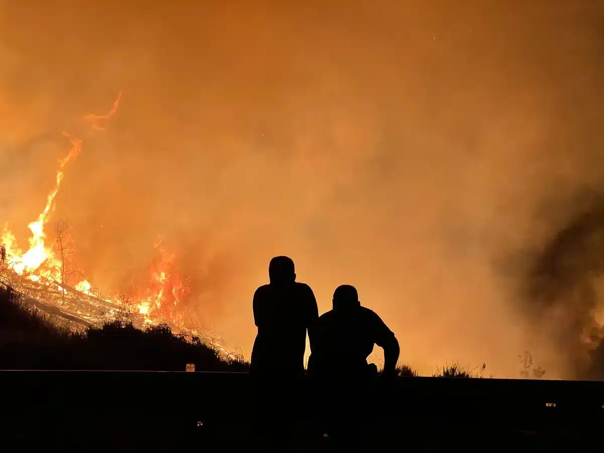 Columna densa de humo elevándose sobre terreno seco con vehículos de emergencia en primer plano