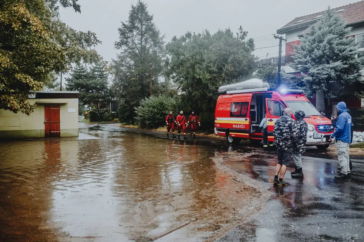 Calle inundada con agua corriendo rápidamente y servicios de emergencia en la zona