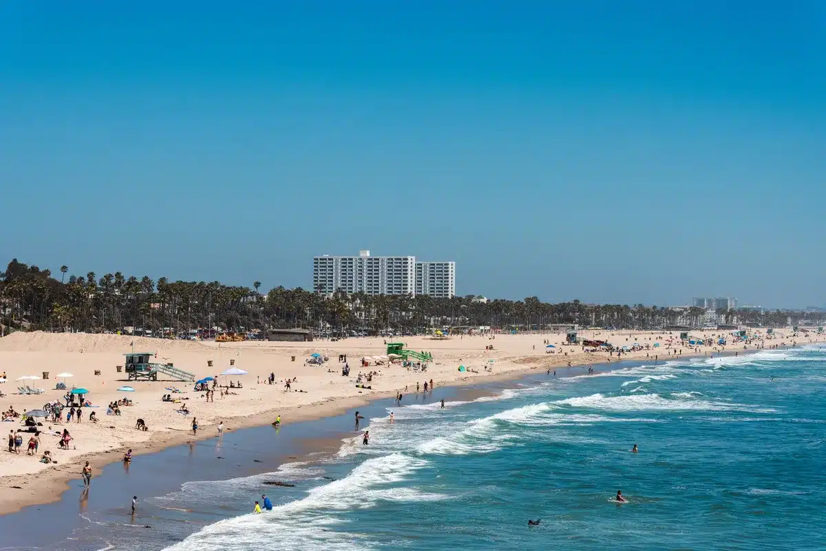 Playa abarrotada en verano con socorristas, personal de limpieza y servicios de seguridad atendiendo a multitudes de tur
