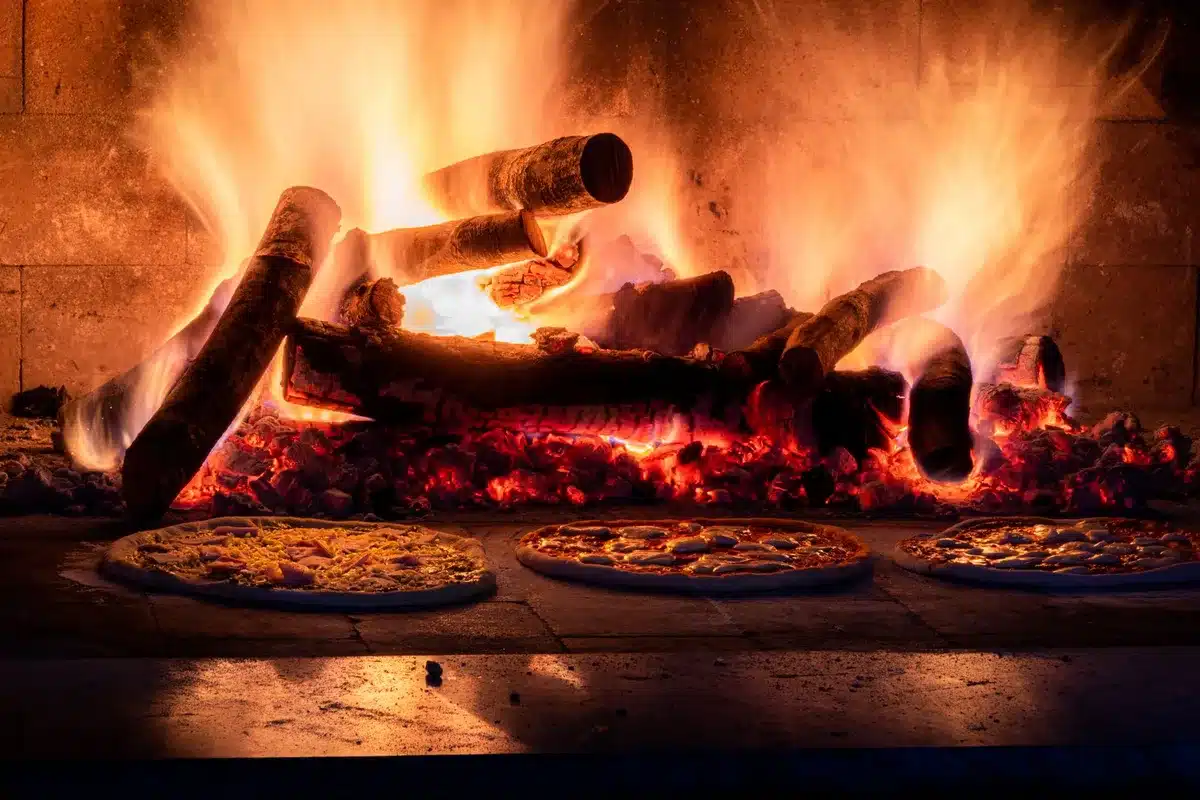 Manos anónimas estirando masa de pizza fresca sobre superficie de trabajo con harina