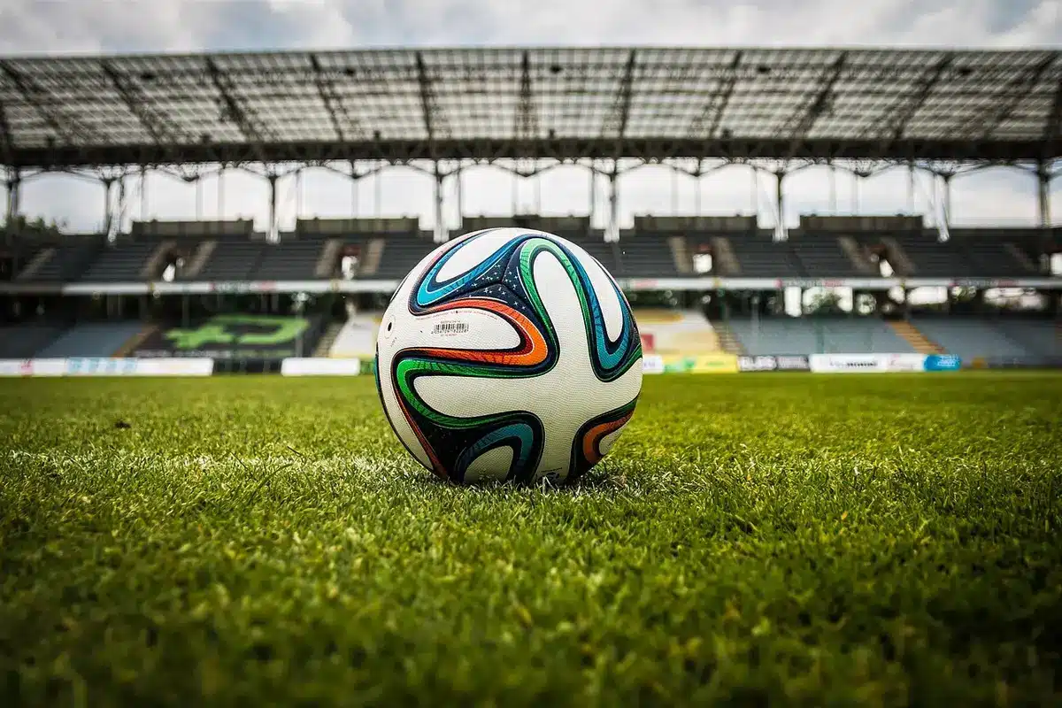 Joven futbolista debutando en el campo con afición y compañeros de fondo