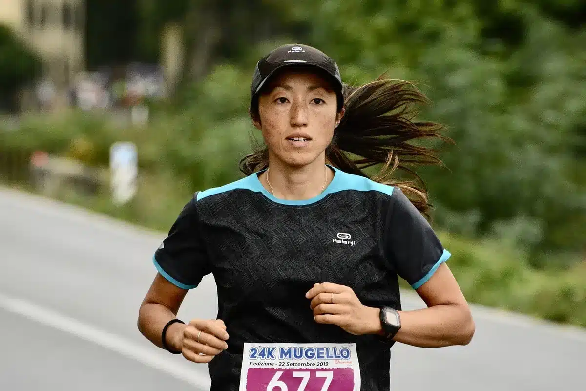 Corredora de maratón en plena carrera sobre un circuito soleado, dominando la prueba con ritmo firme.