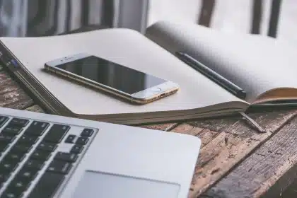 Manos anónimas con móvil y papeles en una mesa de oficina, reflejando notificaciones digitales