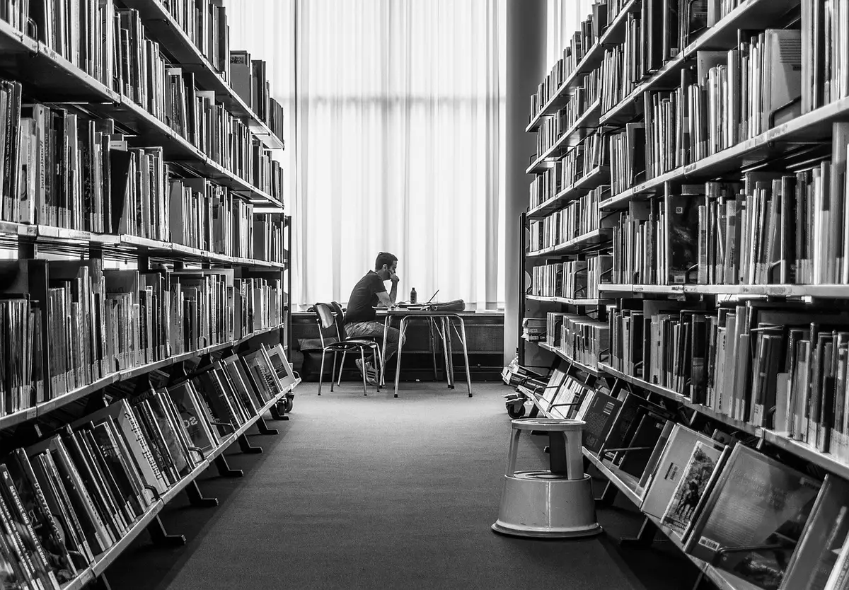 Manos leyendo en una biblioteca que sugieren aprendizaje y espera